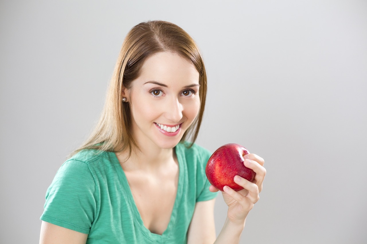 A girl holding a red apple and smiling at the camera