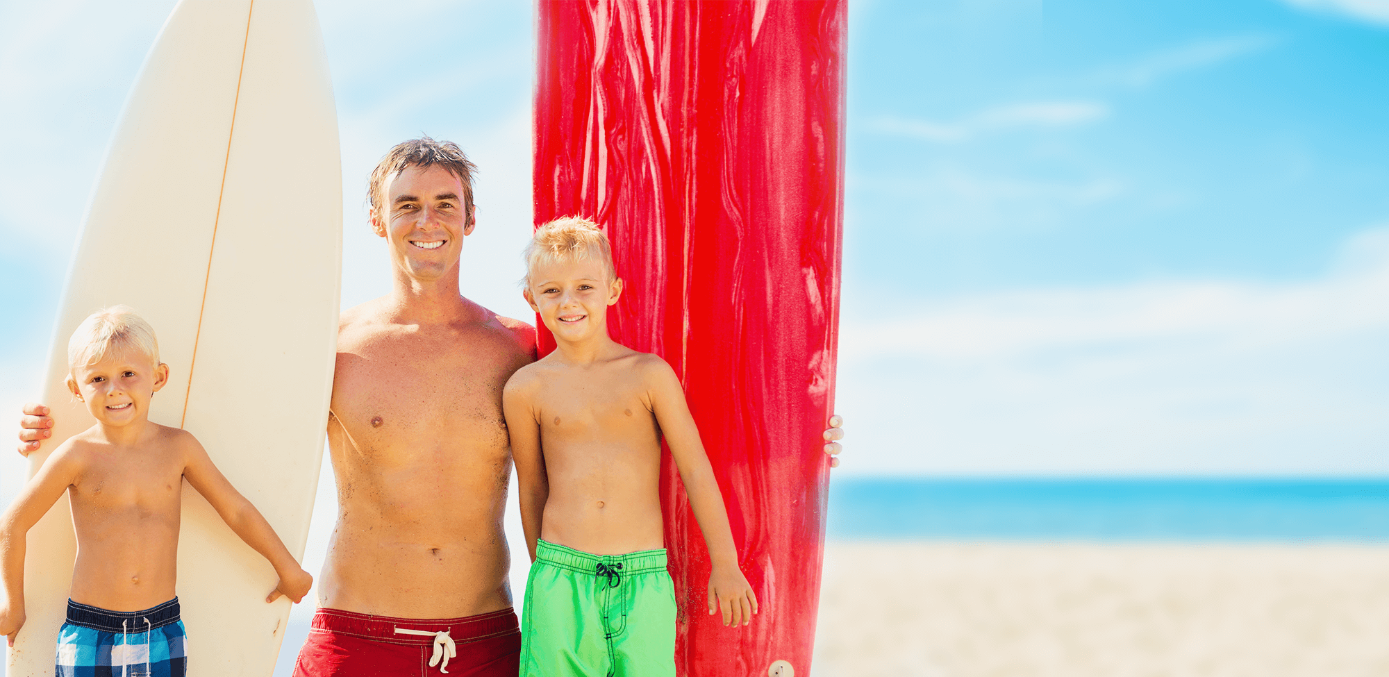 family smiling while holding surfboards on the beach