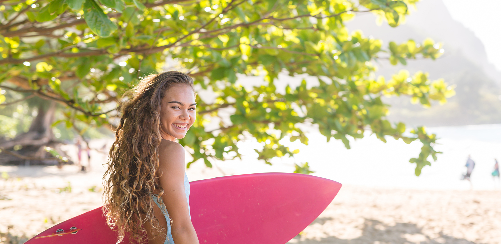 A teen holding her surf board and enjoying her day at the beach.
