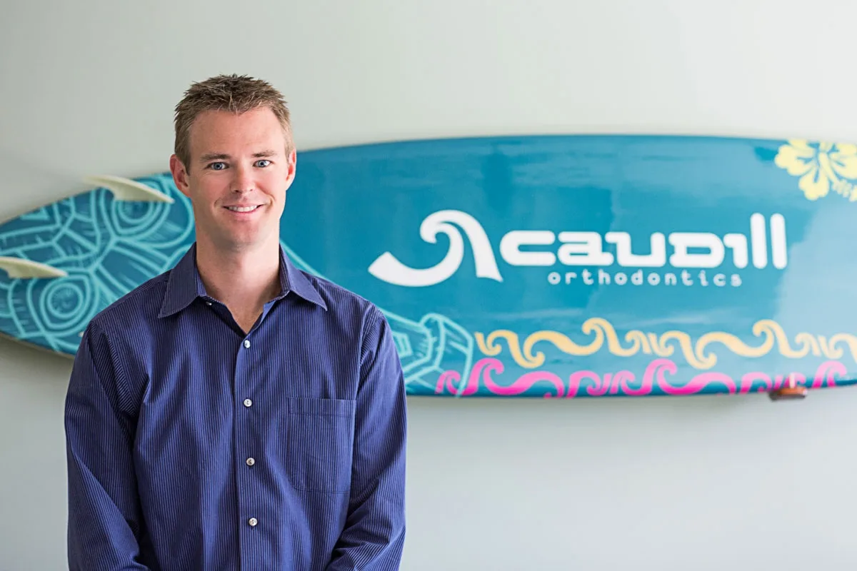 Dr. Caudill posing for a photo with a Caudill surf board at the back