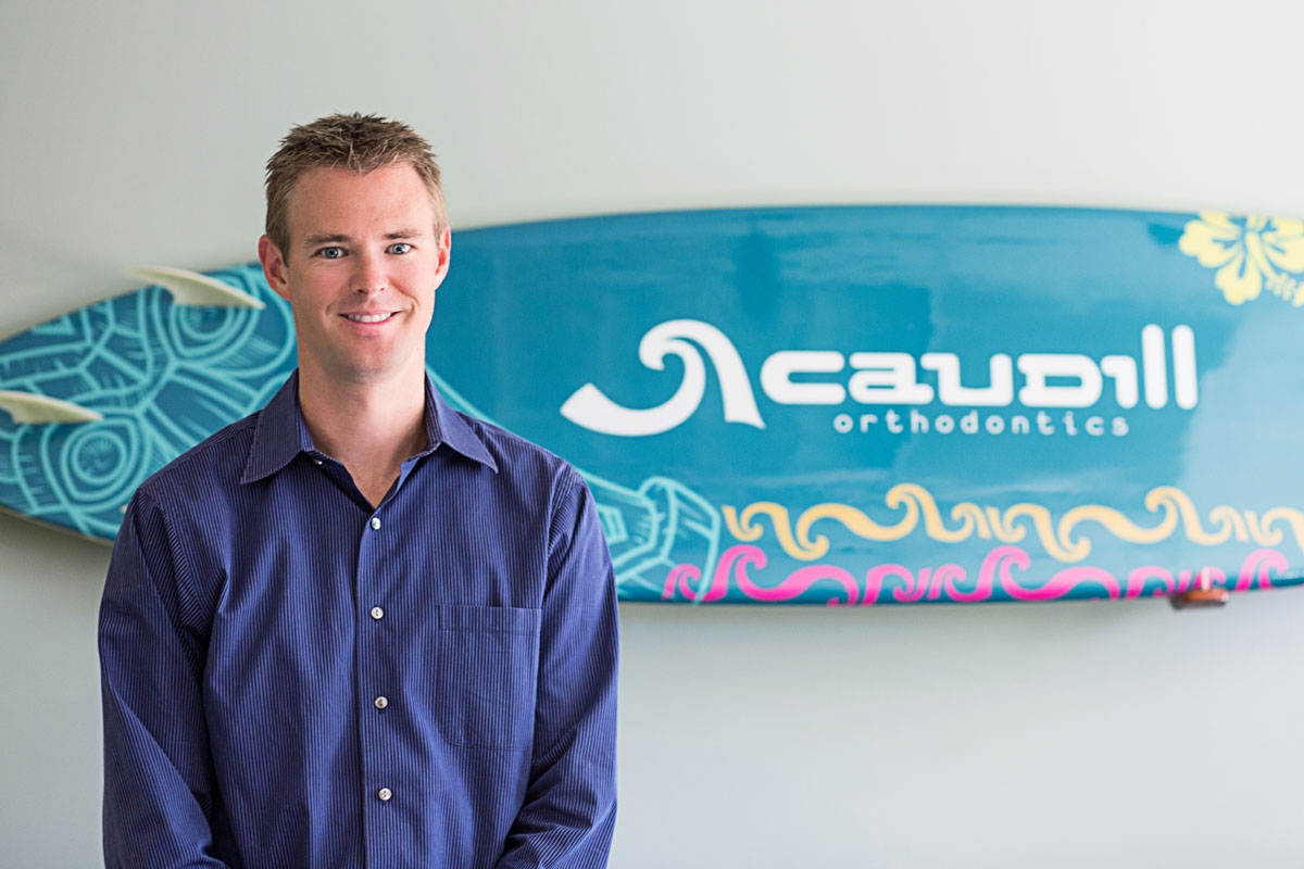 Dr. Caudill posing for a photo with a Caudill surf board at the back