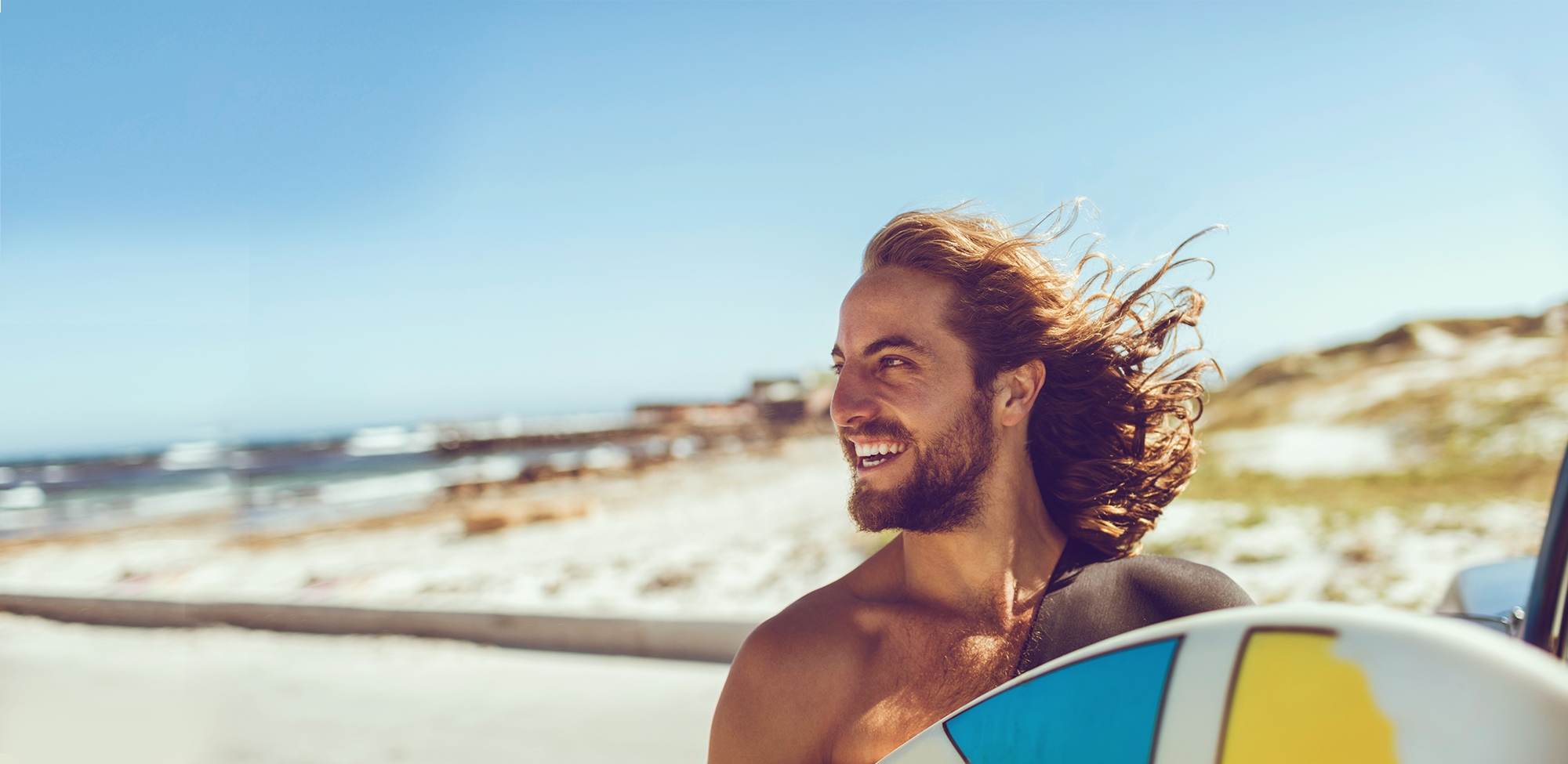 young man smiling while holding surfboard on beach