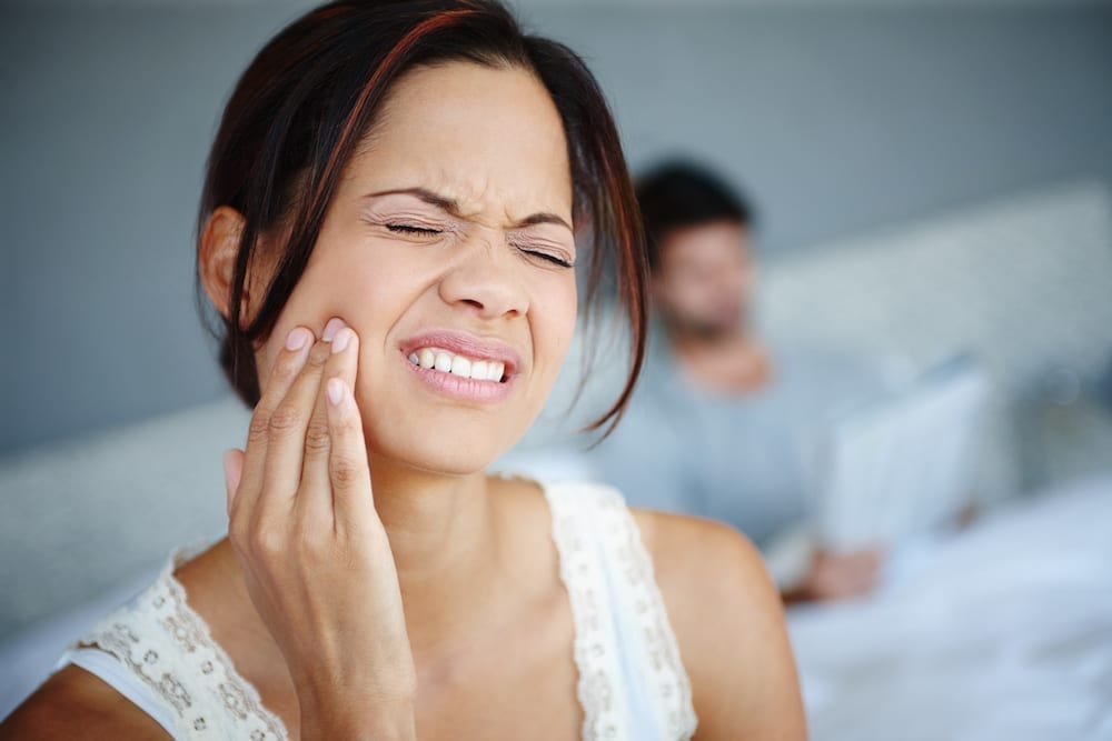 woman holding jaw in pain, when to visit an emergency orthodontist, Caudill & McNeight orthodontics